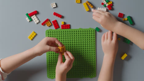 Overhead-Shot-Of-Two-Children-Playing-With-Plastic-Construction-Bricks-On-Grey-Background